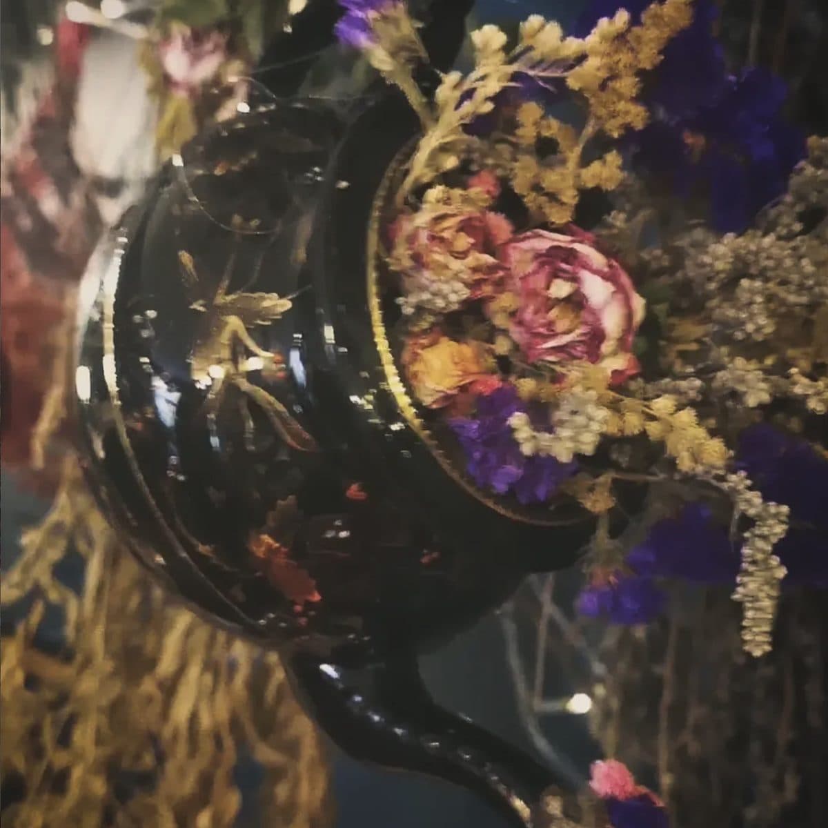 Black ornate teapot bursting with dried roses, golden grasses and purple statice