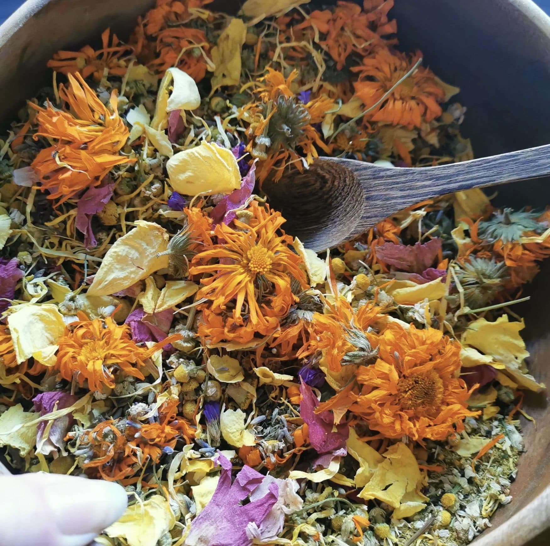 Bowl of dried calendula, chamomile and rose petals with a wooden spoon — Ruby & Elm Herbal Boutique